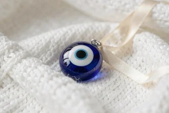 Amulette oeil grec traditionnel en verre bleu cobalt posée sur une couverture de bébé en coton blanc